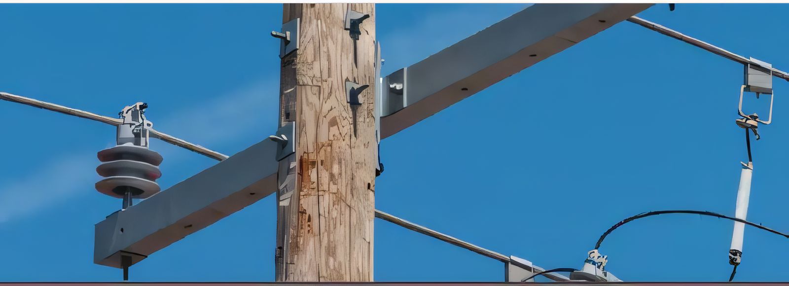 Wooden distribution pole with steel cross-arms, insulators and overhead lines against a clear sky