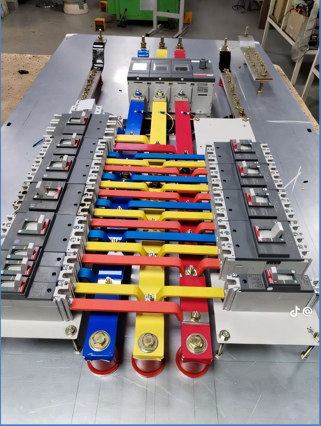 Unmounted three-phase busbar panel assembly laid flat on a workbench, colour-coded copper bars and breakers