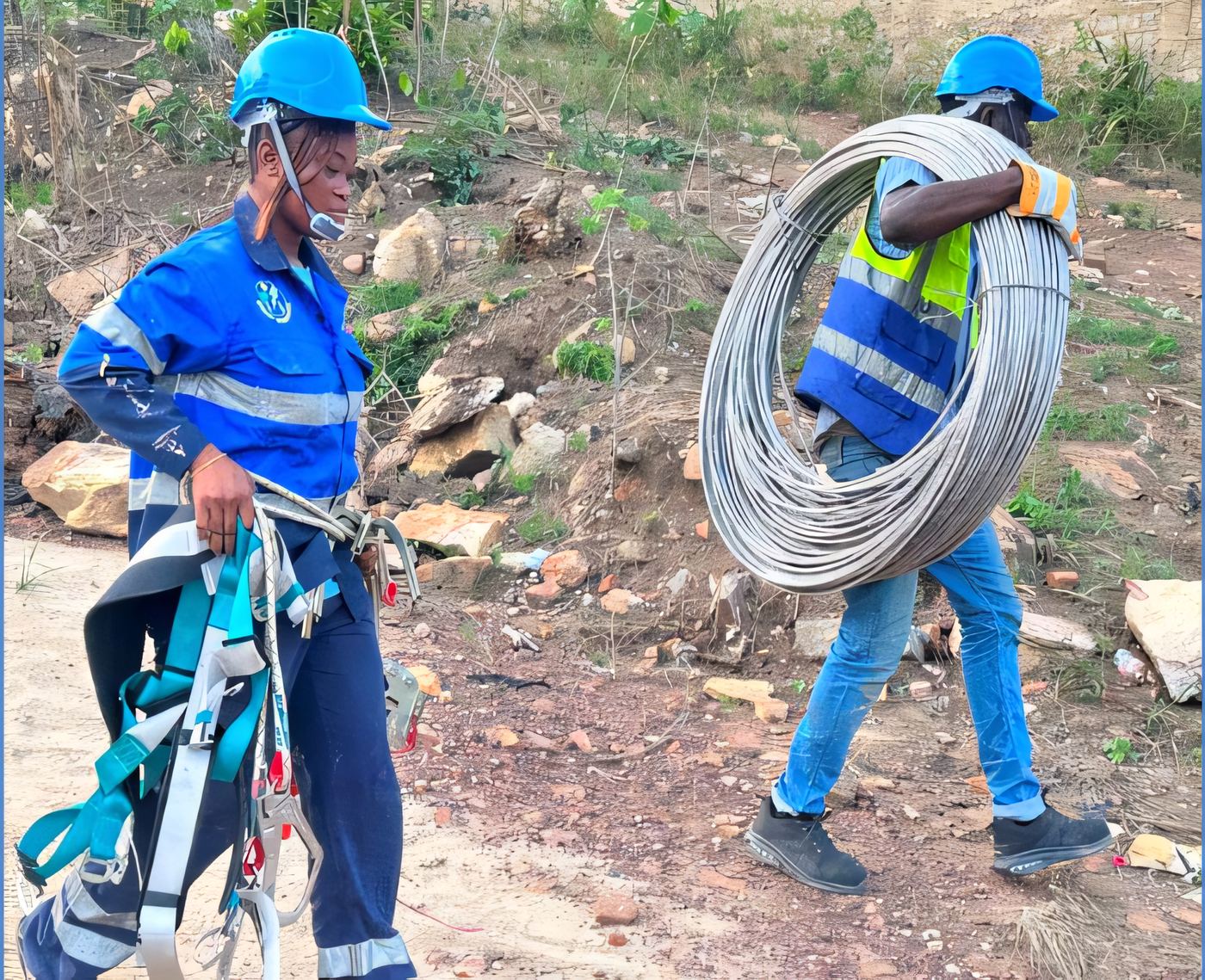 ELSIM linemen carrying a fall-arrest harness and a coil of overhead conductor to a line-works site