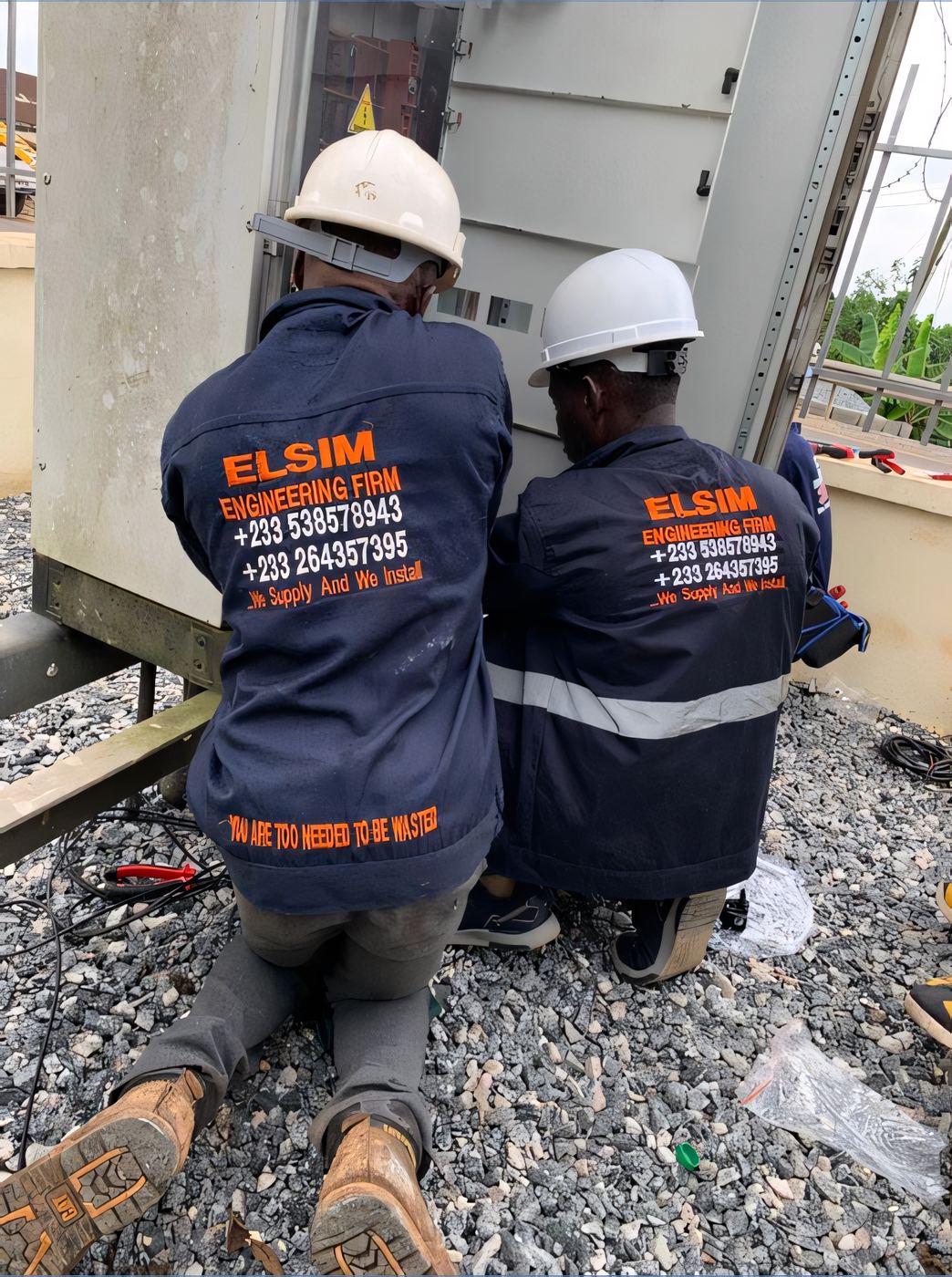 Two ELSIM engineers in hard hats working on an outdoor switchgear cabinet