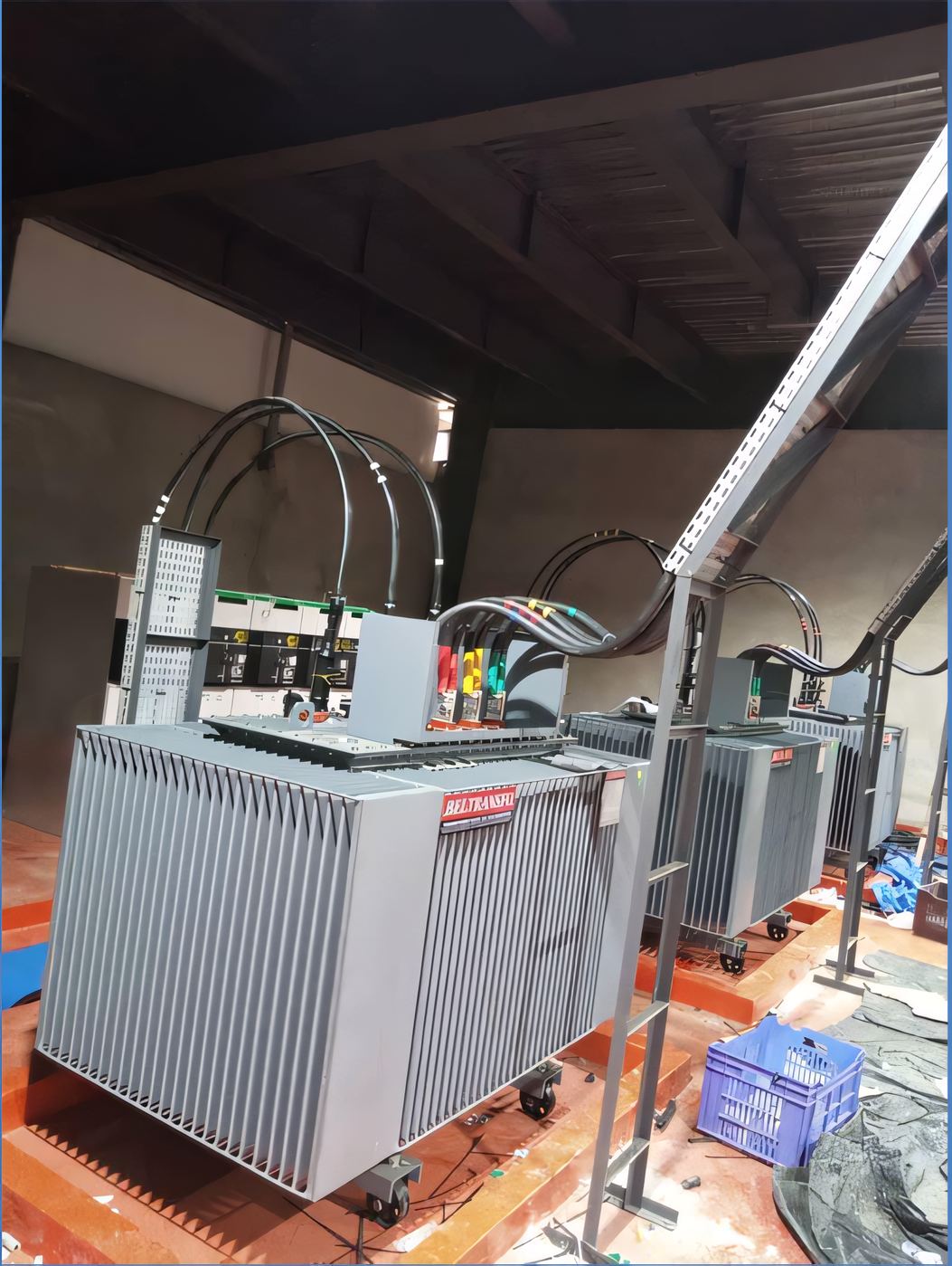 Row of oil-type distribution transformers with copper busbar connections inside a transformer room